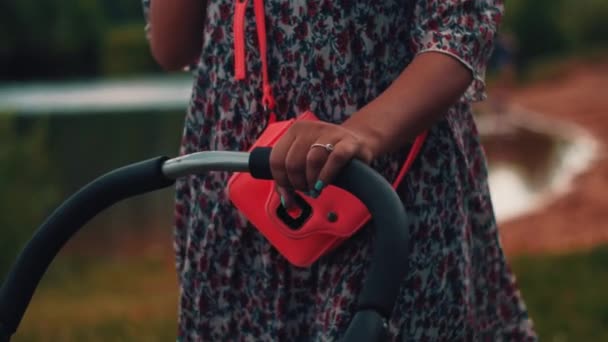 Moeder met kinderwagen lopen en spreken op telefoon in zomer park. — Stockvideo