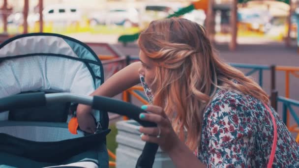 Mère balancez la poussette sur l'aire de jeux pour enfants. Jour d'été. Maternité . — Video