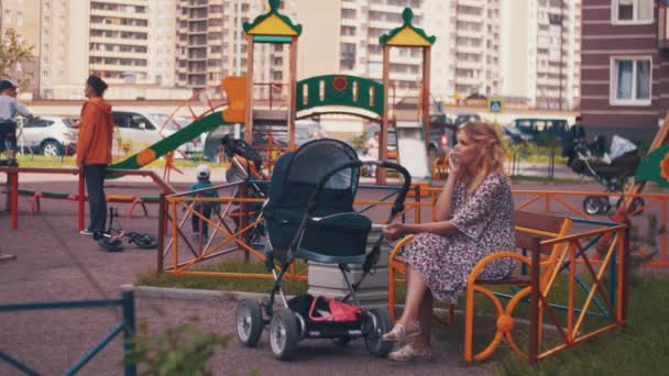 Mor svajar barnvagn på lekplats och tala på telefon. Barn. — Stockvideo