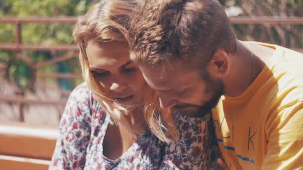 Young in love couple use smartphone sitting on bench. Summer windy day. Chatting — Stock Video