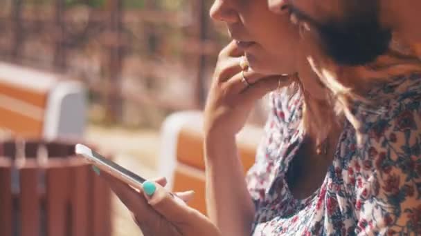 En pareja enamorada con teléfono inteligente sentado en el banco. Día ventoso de verano. Charlando. — Vídeo de stock