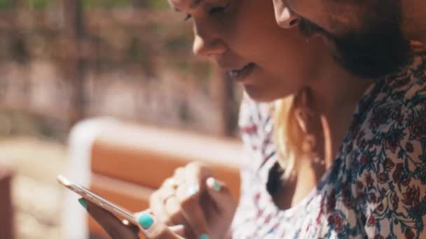 Jeune amoureux couple à l'aide d'un smartphone assis sur le banc. Journée estivale venteuse. Heureux — Video