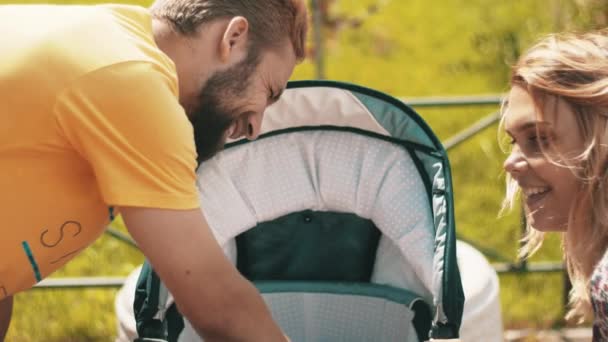 Jovens pais felizes com o bebê na carruagem no banco. Família. Parque infantil — Vídeo de Stock