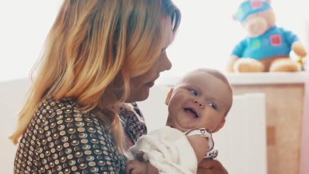 Matka drží malé usměvavé miminko s modrýma očima. Mateřství. Péče. Polibek. — Stock video