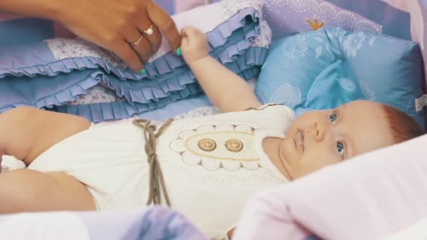 Mère tenir la main petit bébé mensonge dans la crèche regarder des jouets mobiles colorés. Soins . — Video