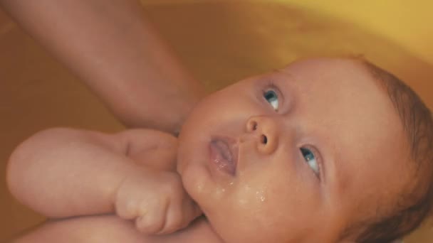 Μητέρα κολυμπά αξιολάτρευτο μωράκι, με γαλάζια μάτια. Κίτρινο μπάνιο. Η μητρότητα. — Αρχείο Βίντεο