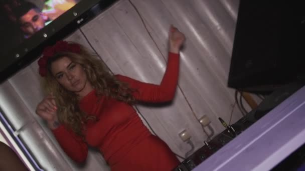 Fröhliches DJ-Mädchen in rotem Kleid mit Rand auf dem Kopf tanzt am Plattenteller im Nachtclub. — Stockvideo