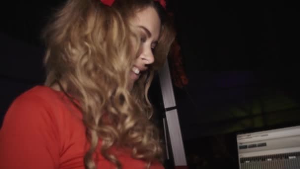 Dj menina em vestido vermelho com aro na cabeça dança na plataforma giratória na festa em boate — Vídeo de Stock