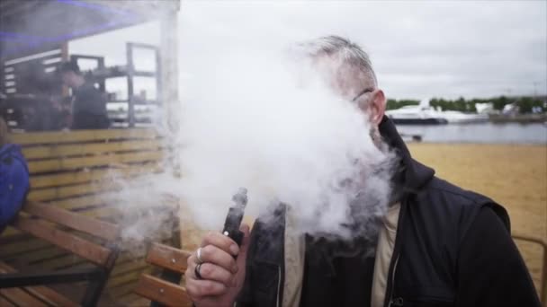 L'uomo in pensione espira molto vapore dalla sigaretta elettronica sul lungomare. Vaper . — Video Stock