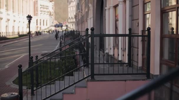 Вид на ганок будинку з залізним парканом. Вулиця, люди, що гуляють, будівлі. Сонячний вечір у місті . — стокове відео
