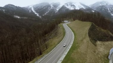 Quadrocopter sinek dağlarda serpantin yol üzerinde. Karlı zirveleri. Araba sürmek.