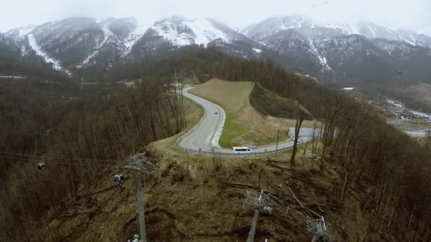 Dron strzelać serpentyn drogi w górach. Samochody. Ośnieżone szczyty. Wyciągi narciarskie — Wideo stockowe