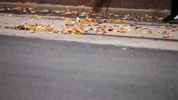 Los pies del conserje barren la hoja amarilla en los rieles del tranvía, corren debido al tranvía . — Vídeo de stock