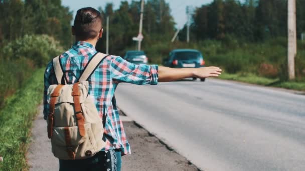 Baksidan ung pojke med ryggsäck lifta på vägen i sommar solig dag. Tumme — Stockvideo