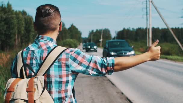 Zadní strana chlapce s batohem stopování na silnici v letní slunečný den. Automobily — Stock video