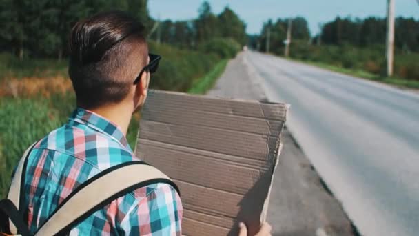 Young boy in sunglasses hitchhiking at road with cardboard plate in summer day. — Stock Video