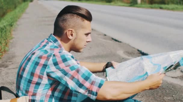 Boy sitting at road looking in map. Waiting. Traveler. Hitchhiking. Cars — Stock Video