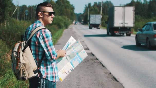 Menino com mochila olhando no mapa na estrada no verão dia ensolarado. Viajante — Vídeo de Stock