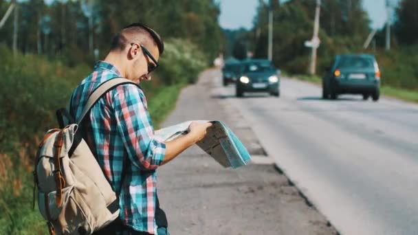 Jongen met kaart en rugzak verblijven tijdens de weg aan de zonnige zomerdag. Toeristische. Auto 's. — Stockvideo