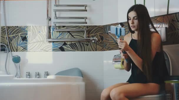 Girl sitting on toilet in bathroom. Take selfie on blue monopod. Posing. — Stock Video