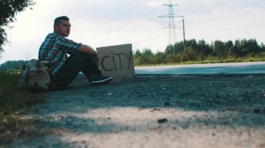 Young boy with backpack sitting at roadside with cardboard plate city. Traveler.
