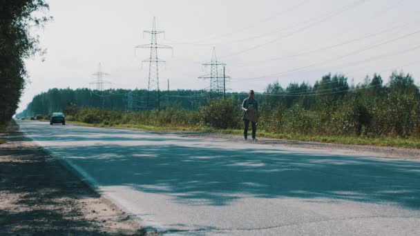 Niño caminando a lo largo de la carretera mantenga placa de cartón con la ciudad signo. Hacer autostop. Viaje. — Vídeos de Stock