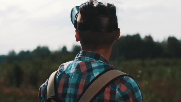 Rapaz com mochila à procura de óculos de realidade virtual. Engraçado. Dia de verão. A brincar. — Vídeo de Stock