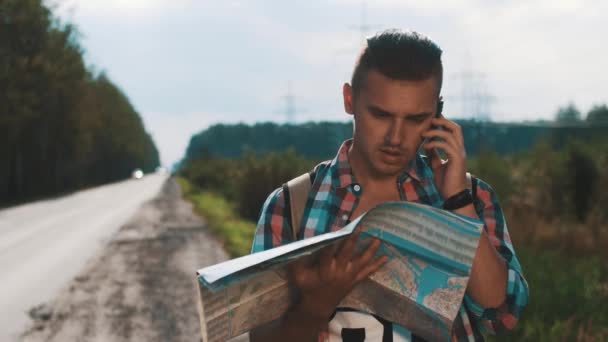 Pojke med ryggsäck letar i karta på väg. Pratar på telefon. Sommar solig dag — Stockvideo