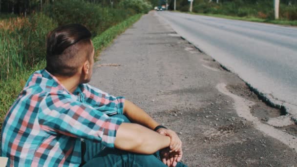 Niño sentado en el camino mantenga la oreja de hierba en la boca. ¡Espera! Viajar. Autoestop — Vídeos de Stock