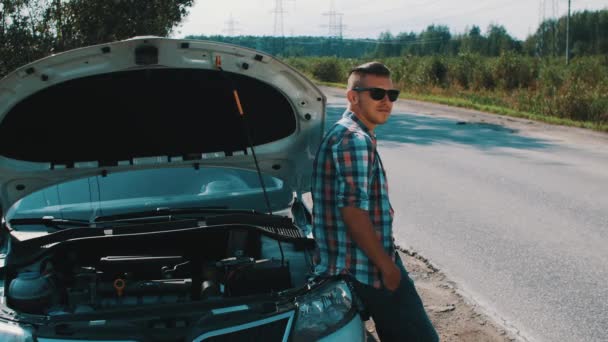 El chico con gafas de sol se queda en el coche roto en la carretera. Hacer autostop. Esperando ayuda — Vídeos de Stock