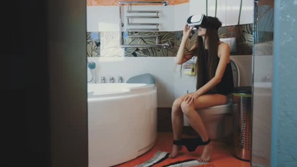 Young girl sit on toilet. Looking in virtual reality glasses. Black underwear — Αρχείο Βίντεο