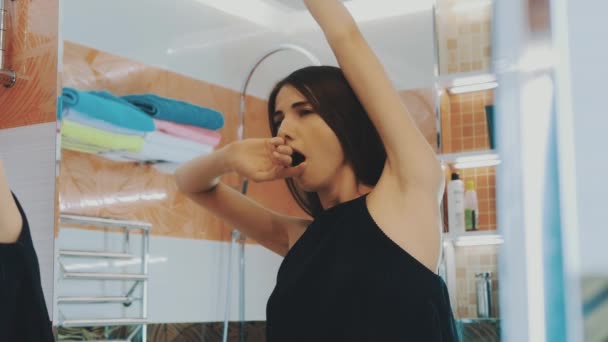 Young brunette girl stretch and yawning in front of mirror in bathroom. Morning. — Wideo stockowe