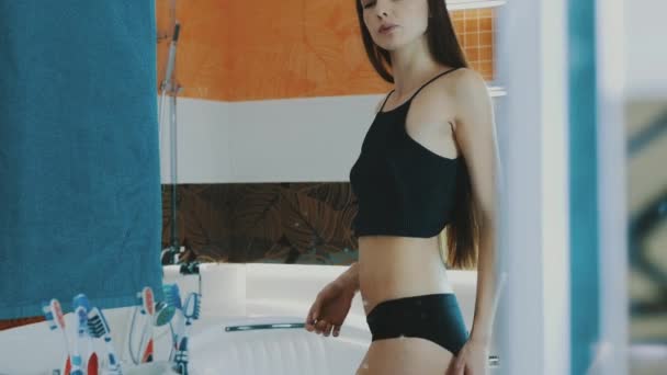 Slim girl in black top checking thigh in front of mirror in bathroom. Shape. — Stock Video