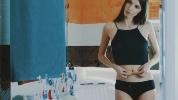 Young girl in black top checking stomach in front of mirror in bathroom. Slim — Stockvideo