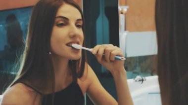 Young brunette girl brush teeth in front of mirror in bathroom. Morning hygiene