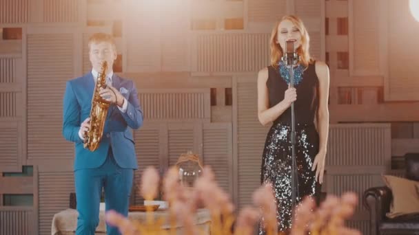 Parıltılı elbiseli caz vokalisti ve mavi takım elbiseli saksafoncu sahnede performans sergiliyor. — Stok video