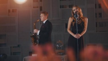 Siyah elbiseli çekici caz vokalisti saksofoncu ile sahne alanı'nda gerçekleştirin. Dans
