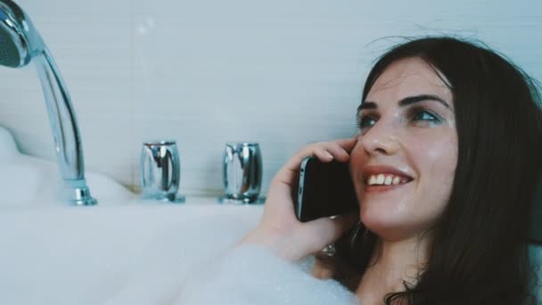 Μελαχρινή κοπέλα λαμβάνοντας μπανιέρα γεμάτη από αφρώδες υλικό. Μιλώντας στο τηλέφωνο. Χαλαρώστε. Ανάπαυσης. — Αρχείο Βίντεο