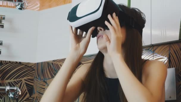 Chica joven sentada en el baño en gafas de realidad virtual en la cabeza. Mirando hacia arriba . — Vídeos de Stock