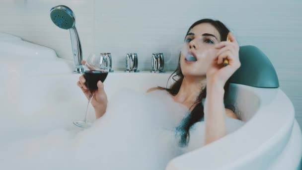 Fille se détendre dans le bain plein de mousse. Smoke cigarette électronique, vapeur, vin rouge . — Video