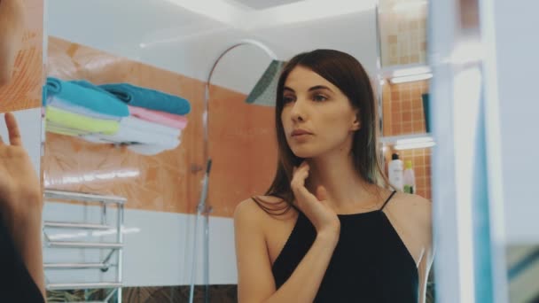 Молода брюнетка дивиться у дзеркало у ванній. Перевірка брів. Краса . — стокове відео