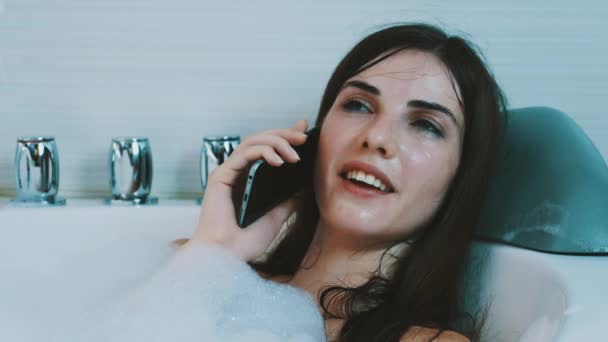 युवा लड़की फोम से भरा स्नान ले रही है। फोन पर बात कर रहा है। आराम करो। आराम करना। मुस्कुराओ — स्टॉक वीडियो