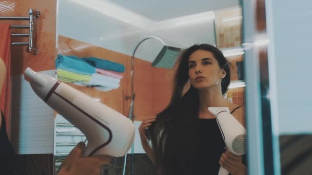 Menina atraente cabelo seco por secador de cabelo no banheiro no espelho. A dançar. Posando — Vídeo de Stock