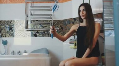 Çekici kız tuvalette banyo ve al selfie mavi monopod üzerinde oturan.