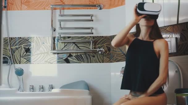 Chica sentarse en el inodoro en gafas de realidad virtual. Cuarto de baño. Juego. Tocar pecho — Vídeos de Stock