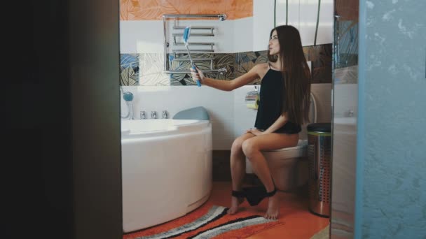 Girl sitting on toilet. Black underwear. Take selfie on blue monopod. Bathroom — Stock Video