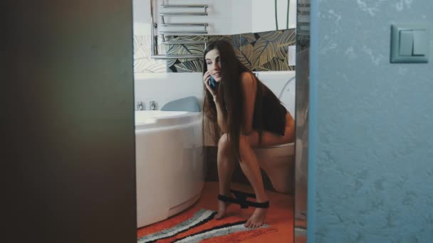 Chica joven sentada en el inodoro sin ropa interior hablando por teléfono. Cuarto de baño — Vídeos de Stock