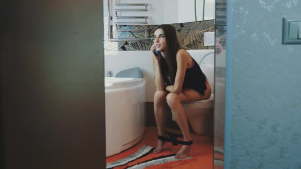 Young girl sitting on toilet. Black underwear. Talking on phone. Restriim. Smile — 图库视频影像