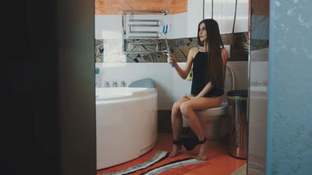 Ragazza seduta sul water in bagno. Biancheria intima nera. Fatti un selfie su un monopiede blu — Video Stock