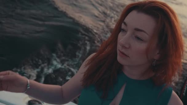 Pretty red hair girl in turquoise dress on motor boat. Evening. Touch hair. — Stock Video